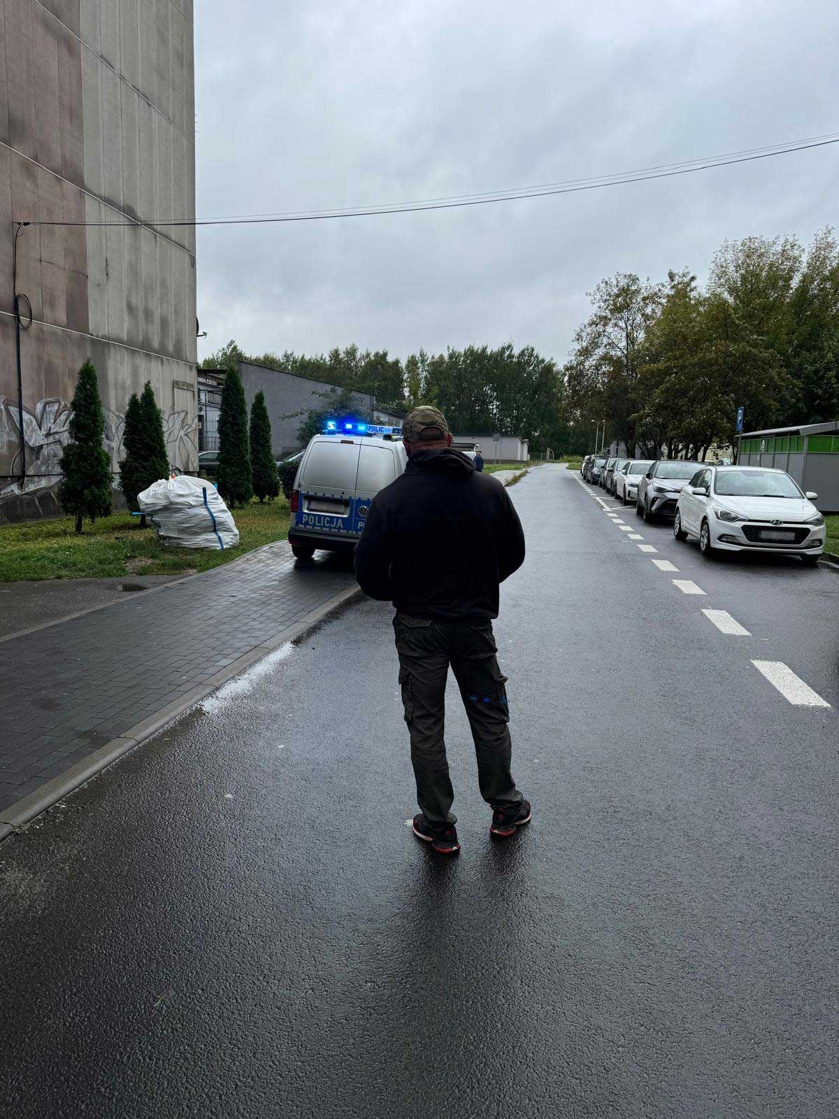 Detektyw na ulicy podczas poszukiwań, w tle radiowóz Policji